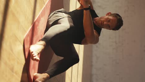 Vertikales-Video-Eines-Mannes-In-Schwarzer-Sport-Sommeruniform,-Der-Auf-Einer-Speziellen-Roten-Matte-In-Der-Sonnigen-Halle-Übungen-Zum-Pumpen-Der-Bauchmuskeln-Macht