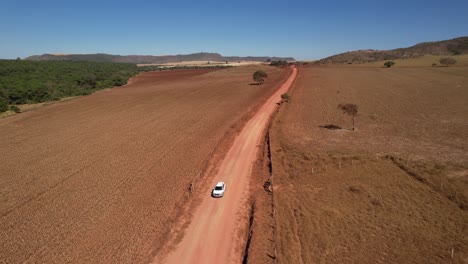 drone-view-of-a-moving-car-raising-dust-on-a-dirt-road-in-Chapada-dos-Veadeiros,-Goiás,-Brazil-sunny-day