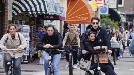 Long-shot-of-people-on-bikes-cycling-on-a-busy-street-in-Amsterdam,-the-Netherlands