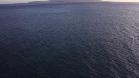 Low-tilting-up-aerial-shot-of-the-sacred-island-of-Kaho'olawe-and-Molokini-Crater-from-Wailea-during-sunset-in-West-Maui,-Hawai'i