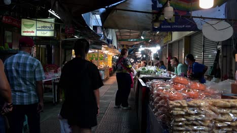 Local-and-foreign-tourists-on-a-late-night-tour-of-the-Amphawa-Floating-Night-Market-walking-street,-looking-for-some-souvenirs-and-food-to-eat