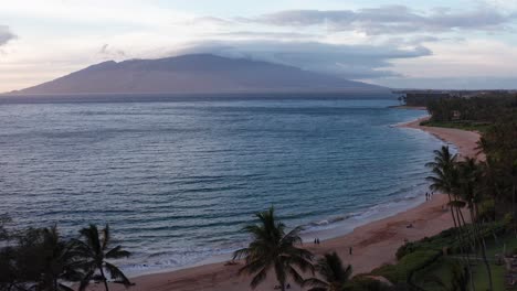 Low-panning-aerial-shot-of-the-pristine-beaches-of-Wailea-with-West-Maui-in-the-distance-at-sunset-in-Hawai'i