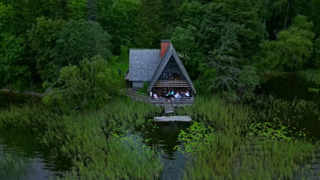 Close-up-of-a-drone-shot-of-a-house-on-a-lake-with-people-celebrating-and-waving-to-the-camera