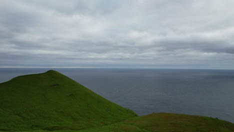 Upward-aerial-revealing-lush-green-mountainous-Kalsoy-Island-meadow-near-ocean