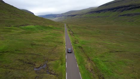 Aerial-tracking-of-electric-car-on-remote-Faroe-Islands-road,-cloudy