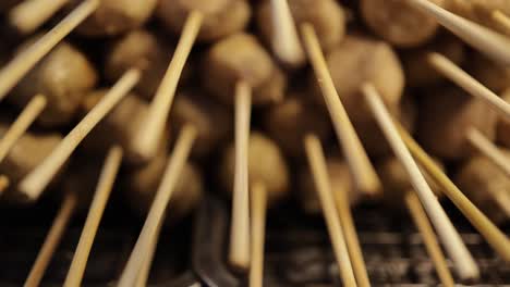 Close-up,-panning-shot-of-grilled-meatball-on-skewers-stacked-on-hot-charcoal-grill-at-street-food-stall