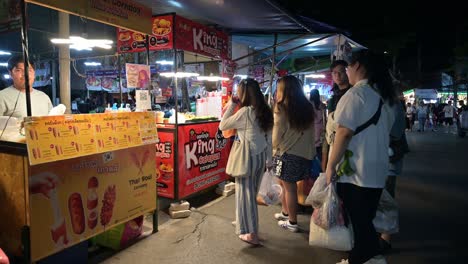 Waiting-for-their-orders-of-fried-octopus,-a-group-of-tourists-are-standing-in-front-of-the-food-stalls-in-Chatuchak-Weekend-Market,-in-Bangkok,-Thailand