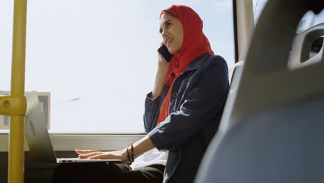 Mujer-Con-Hijab-Hablando-Por-Teléfono-Móvil-Mientras-Usa-Una-Computadora-Portátil-4k