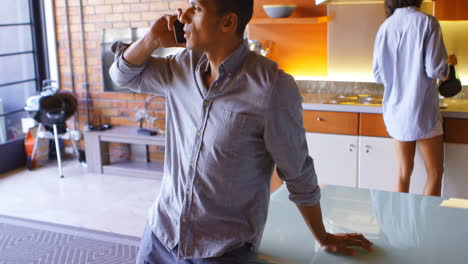 Man-talking-on-mobile-phone-while-his-partner-preparing-coffee-in-background-4k