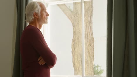 Senior-man-looking-through-window-in-bedroom-at-home-4k