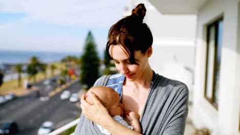 Young-smiling-mother-standing-in-balcony-with-baby-in-sling-4k