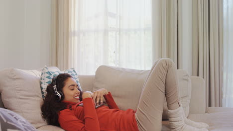 Glückliche-Frau,-Die-Auf-Dem-Sofa-Liegt-Und-Ein-Tablet-Benutzt,-Während-Sie-Musik-Auf-Ihren-Kopfhörern-4k-4k-Genießt