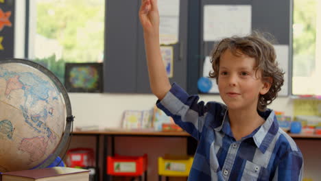 Front-view-of-Caucasian-schoolboy-raising-hand-on-desk-in-classroom-at-school-4k