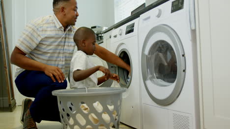 Side-view-of-mid-adult-black-father-and-son-washing-clothes-in-washing-machine-at-comfortable-home-4