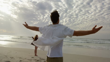 Rear-view-of-young-couple-standing-with-arms-outstretched-and-looking-at-sea-on-the-beach-4k
