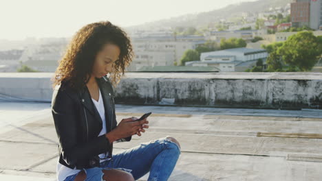 Fashionable-young-woman-on-urban-rooftop-using-smartphone