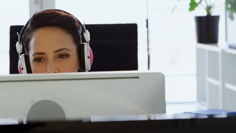 Front-view-of-Caucasian-Businesswoman-in-headphones-working-on-computer-at-desk-in-office-4k