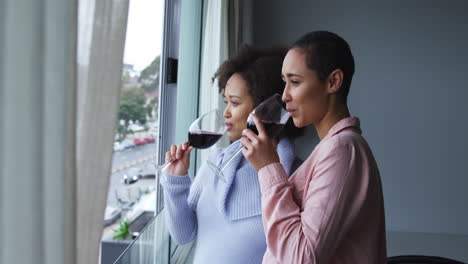 Lesbian-couple-drinking-red-wine-at-window