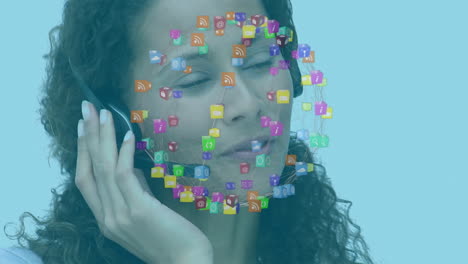 Animation-of-mixed-race-woman-wearing-a-headset-and-using-a-computer-over-social-icons