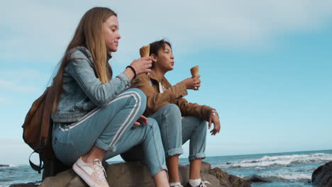 Side-view-of-a-Caucasian-and-a-mixed-race-girl-eating-ice-cream-seaside