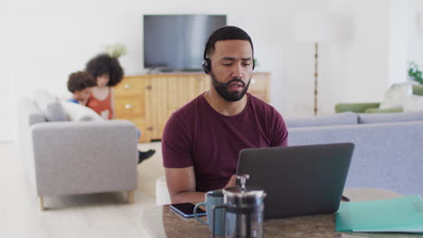Man-wearing-headset-talking-on-phone-while-using-laptop-at-home