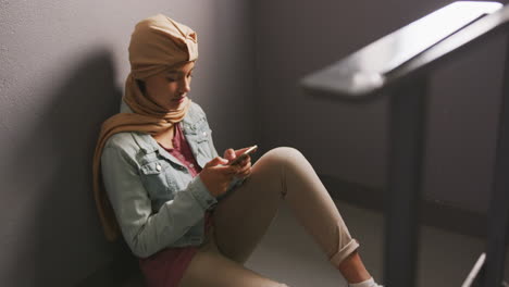 Asiatische-Studentin-Trägt-Einen-Beigen-Hijab,-Lehnt-An-Einer-Wand-Und-Benutzt-Ein-Smartphone