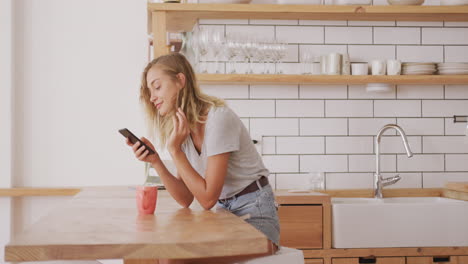 Woman-adjusting-her-hair-behind-her-ear-while-using-smart-phone-at-home