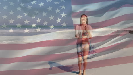 Animation-of-American-flag-waving-over-happy-woman-jumping-dancing-on-beach-by-seaside