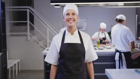 Caucasian-female-cook-working-in-a-restaurant-kitchen-looking-at-camera-and-smiling
