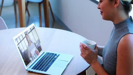 Creative-business-woman-holding-coffee-cup-having-a-video-meeting-on-her-laptop