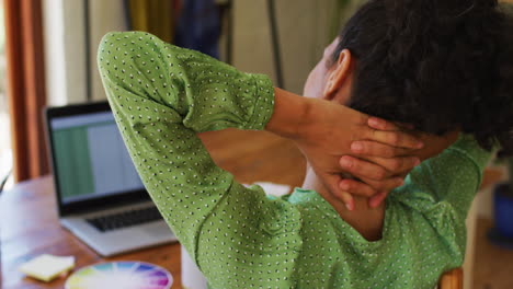 Mixed-race-woman-stretching-her-neck-while-working-from-home