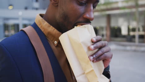 African-american-businessman-eating-sandwich-in-city-street