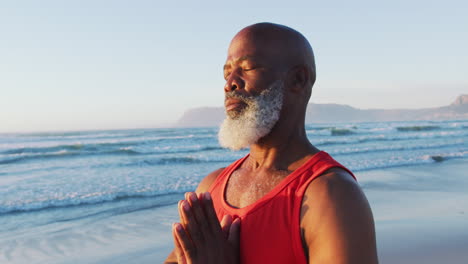 Senior-african-american-man-practising-yoga-with-eyes-closed-at-the-beach