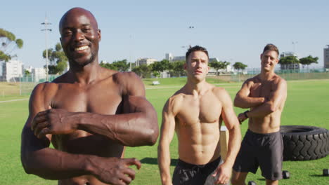 Three-shirtless-diverse-fit-men-smiling-and-turning-to-camera-after-exercising-outdoors
