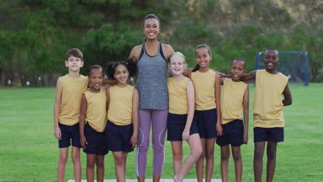 Portrait-of-mixed-race-female-teacher-and-diverse-group-of-schoolchildren-smiling-embracing-outdoors