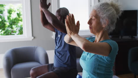 Mixed-race-senior-couple-practicing-yoga-together-in-the-living-room-at-home