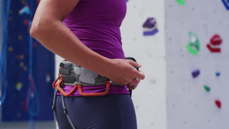 Caucasian-woman-preparing-climbing-harness-belt-for-climb-at-indoor-climbing-wall