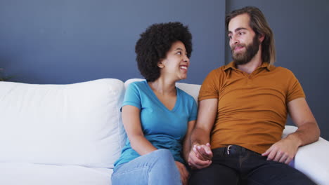 Portrait-of-mixed-race-couple-holding-hands-while-sitting-on-the-couch-at-home