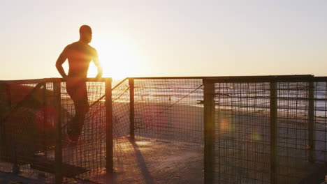 Focused-african-american-man-running-up-stairs,-exercising-outdoors-by-seaside-at-sunset