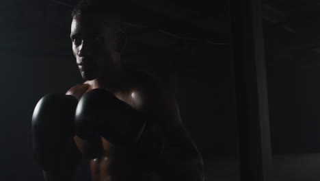 Afroamerikanischer-Mann-Mit-Boxhandschuhen,-Der-In-Einem-Dunklen-Raum-Die-Fäuste-Zusammenschlägt