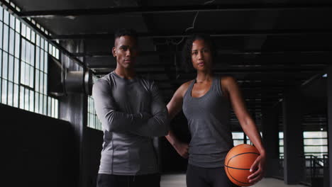 African-american-man-and-woman-standing-in-an-empty-building-holding-a-basketball