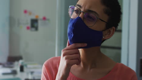 Thoughtful-caucasian-woman-wearing-face-mask-with-hand-on-chin-at-modern-office