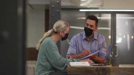 Caucasian-male-and-female-business-colleagues-wearing-masks-in-discussion-at-work