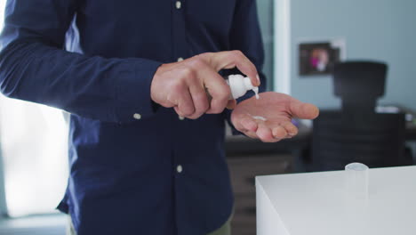 Mid-section-of-man-using-hands-sanitizer-at-modern-office