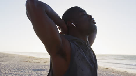 Focused-african-american-man-stretching-with-eyes-closed,-exercising-outdoors-by-seaside