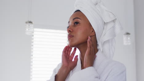African-american-woman-in-bathrobe-touching-her-face-in-the-bathroom