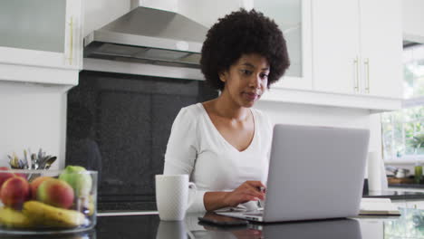 Mujer-Afroamericana-Usando-Una-Computadora-Portátil-En-La-Cocina-Mientras-Trabaja-Desde-Casa