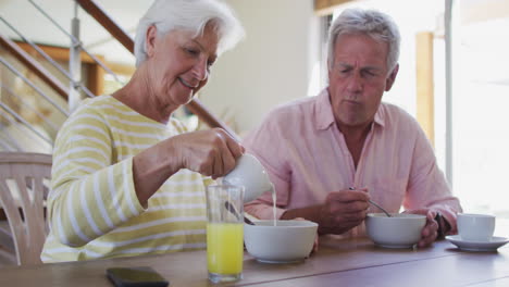 Senior-caucasian-couple-pouring-milk-in-cereal-bowl-having-breakfast-together-at-home