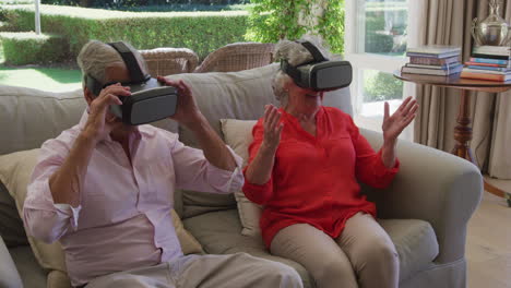Caucasian-senior-couple-sitting-on-couch-in-living-room-using-vr-headsets