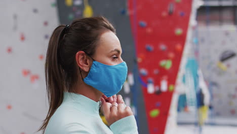 Portrait-of-smiling-caucasian-woman-adjusting-face-mask-at-an-indoor-climbing-gym